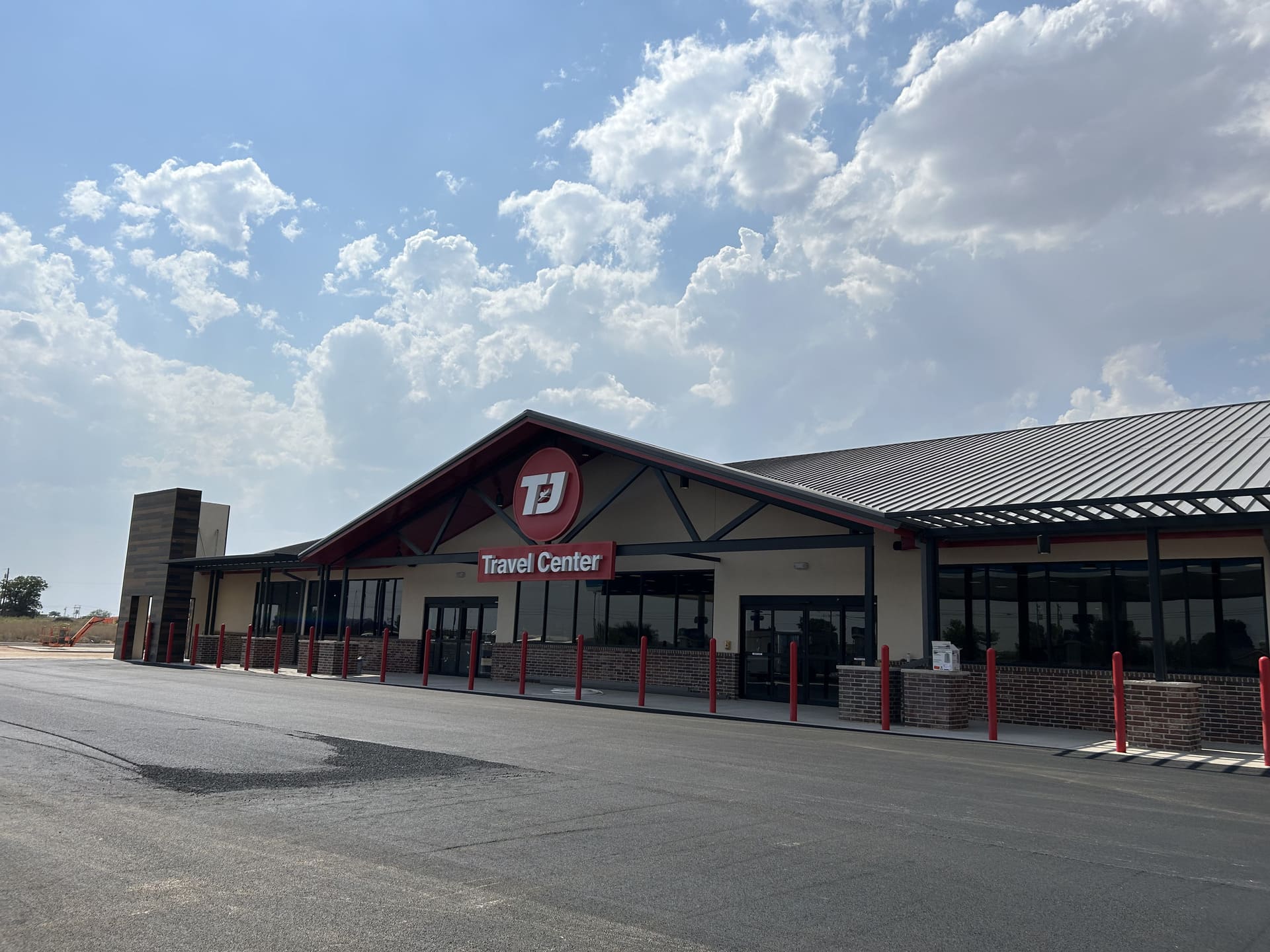 A freshly coated asphalt lot in front of a TJ Travel Center in Texas, with crisp striping and a smooth surface under a bright, partly cloudy sky.