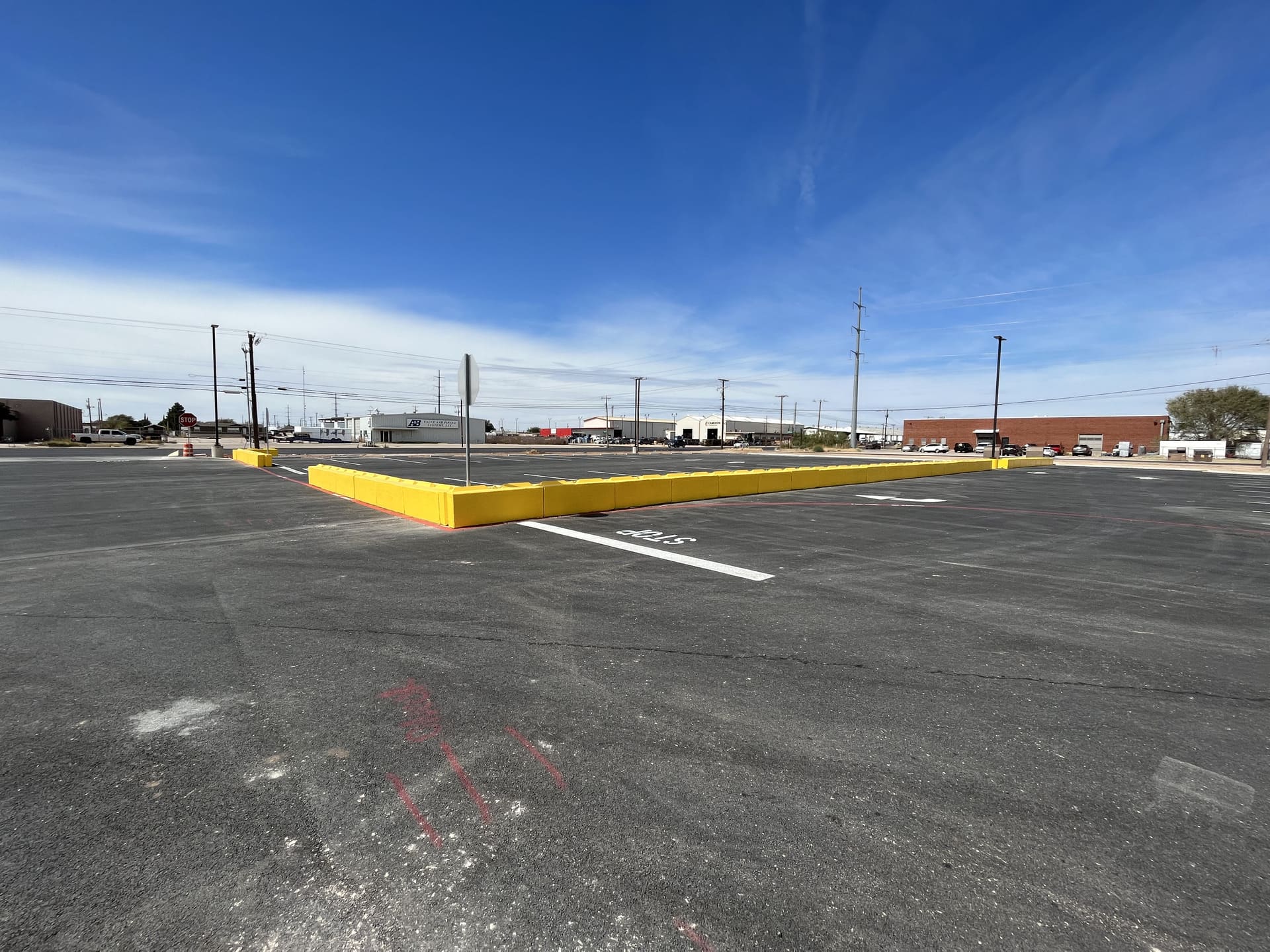 Aerial view of a freshly paved institutional asphalt parking lot with clearly marked white parking lines, directional arrows, and designated parking stalls adjacent to a commercial or educational building.