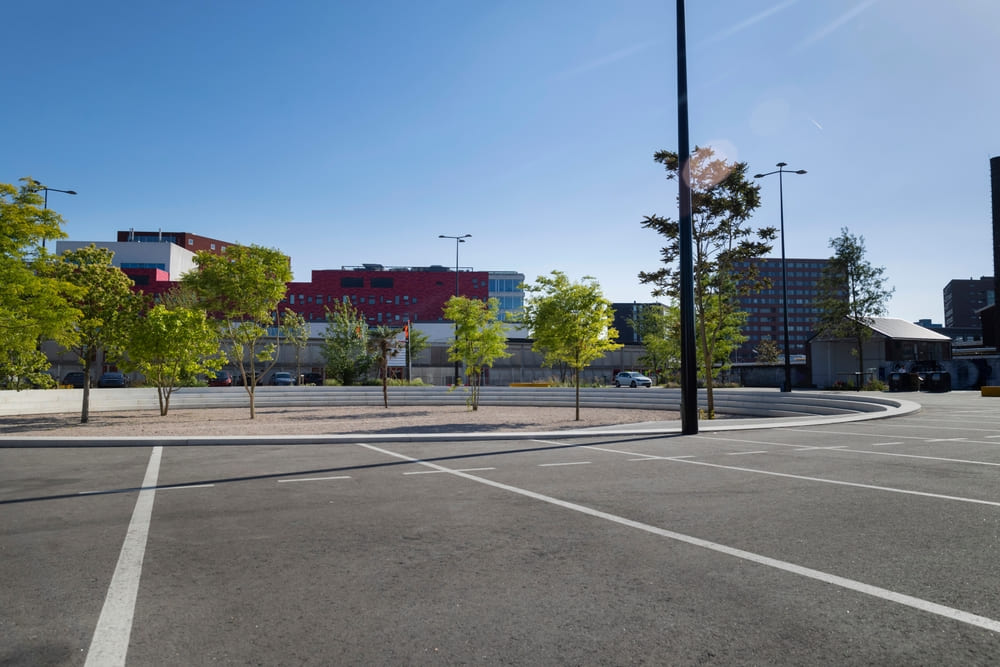 Newly Paved Institutional Parking Lot with Tree-Lined Medians and City Infrastructure in Background