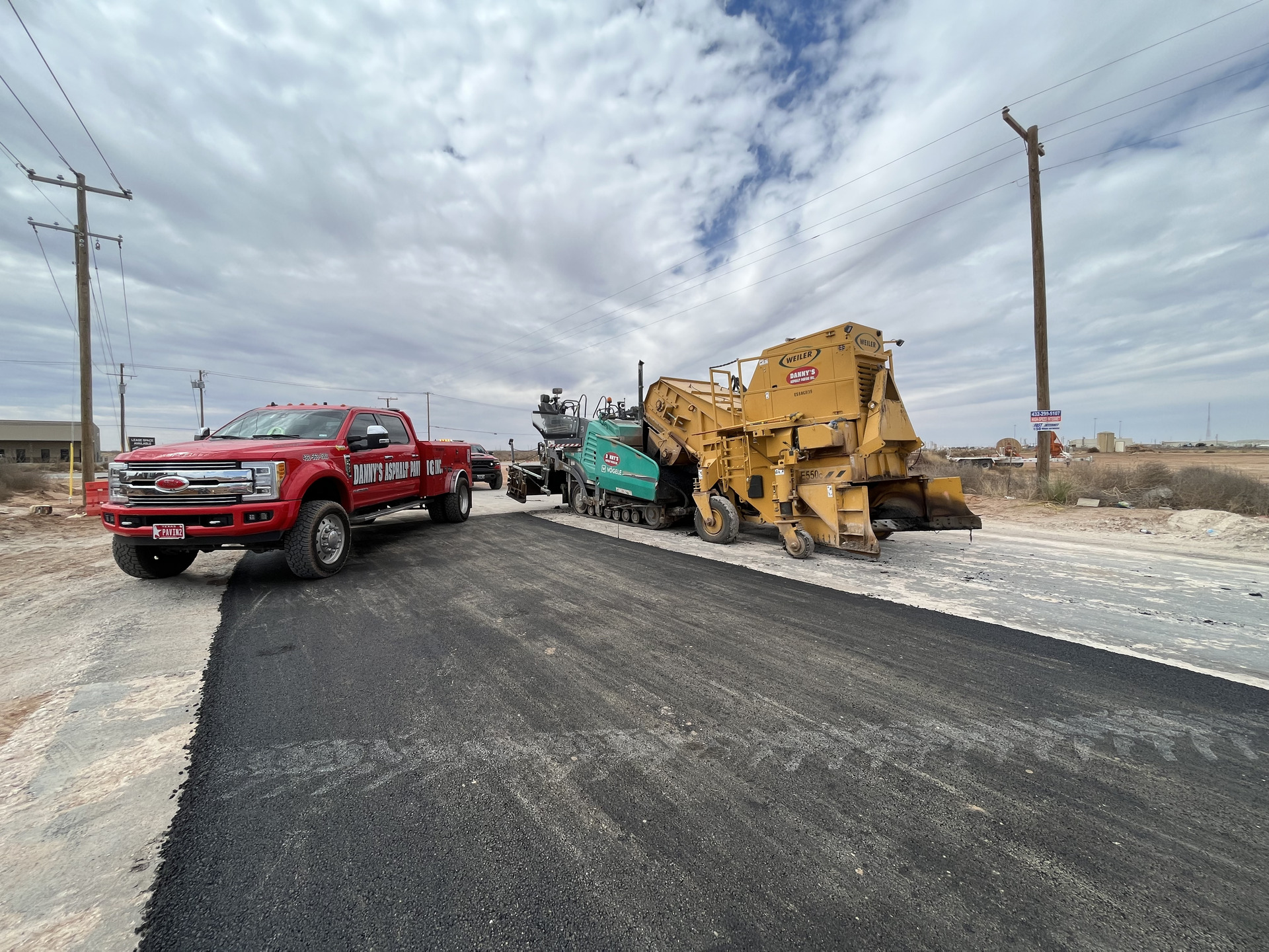 Aerial view of a freshly paved institutional asphalt parking lot with clearly marked white parking lines, directional arrows, and designated parking stalls adjacent to a commercial or educational building.