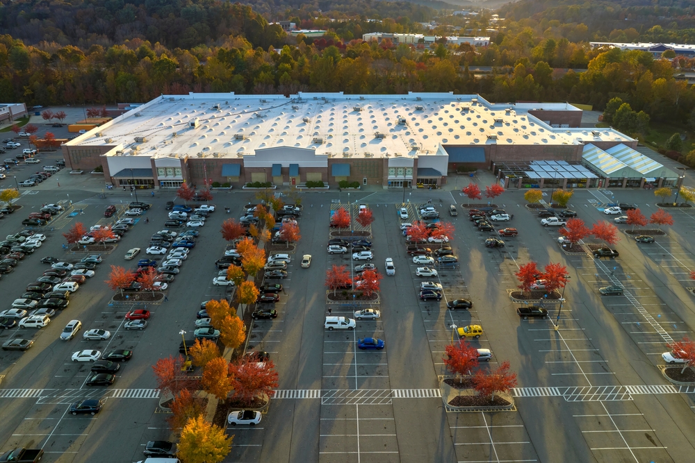 Aerial view of a freshly paved institutional asphalt parking lot with clearly marked white parking lines, directional arrows, and designated parking stalls adjacent to a commercial or educational building.