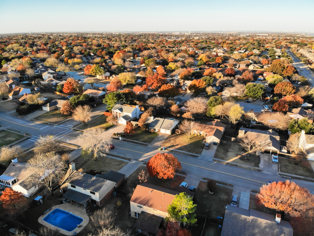 Aerial view of a residential neighborhood with tree-lined streets, single-family homes, and connected roadways, showing a well-established subdivision with paved streets and fall foliage across the community.