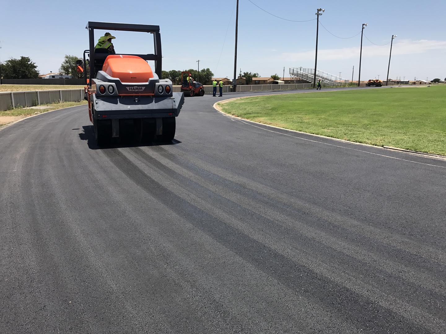 Aerial view of a freshly paved institutional asphalt parking lot with clearly marked white parking lines, directional arrows, and designated parking stalls adjacent to a commercial or educational building.