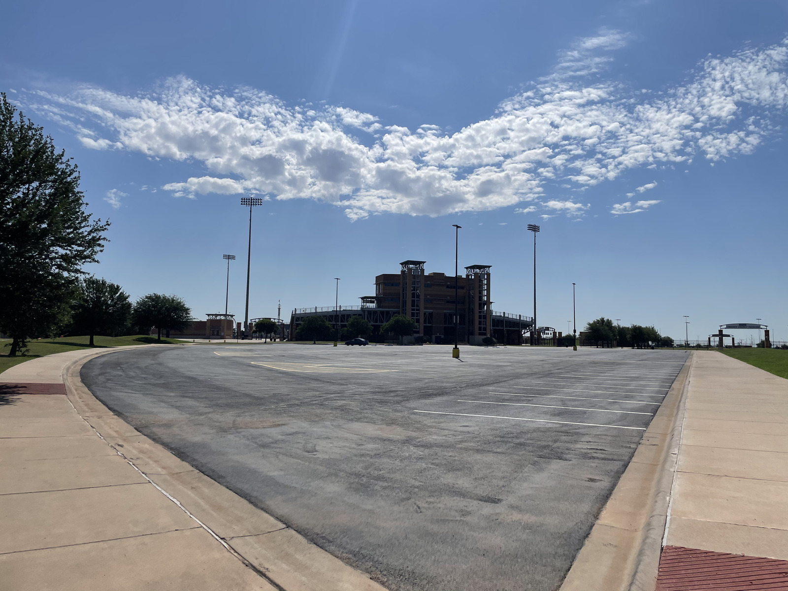 Aerial view of a freshly paved institutional asphalt parking lot with clearly marked white parking lines, directional arrows, and designated parking stalls adjacent to a commercial or educational building.