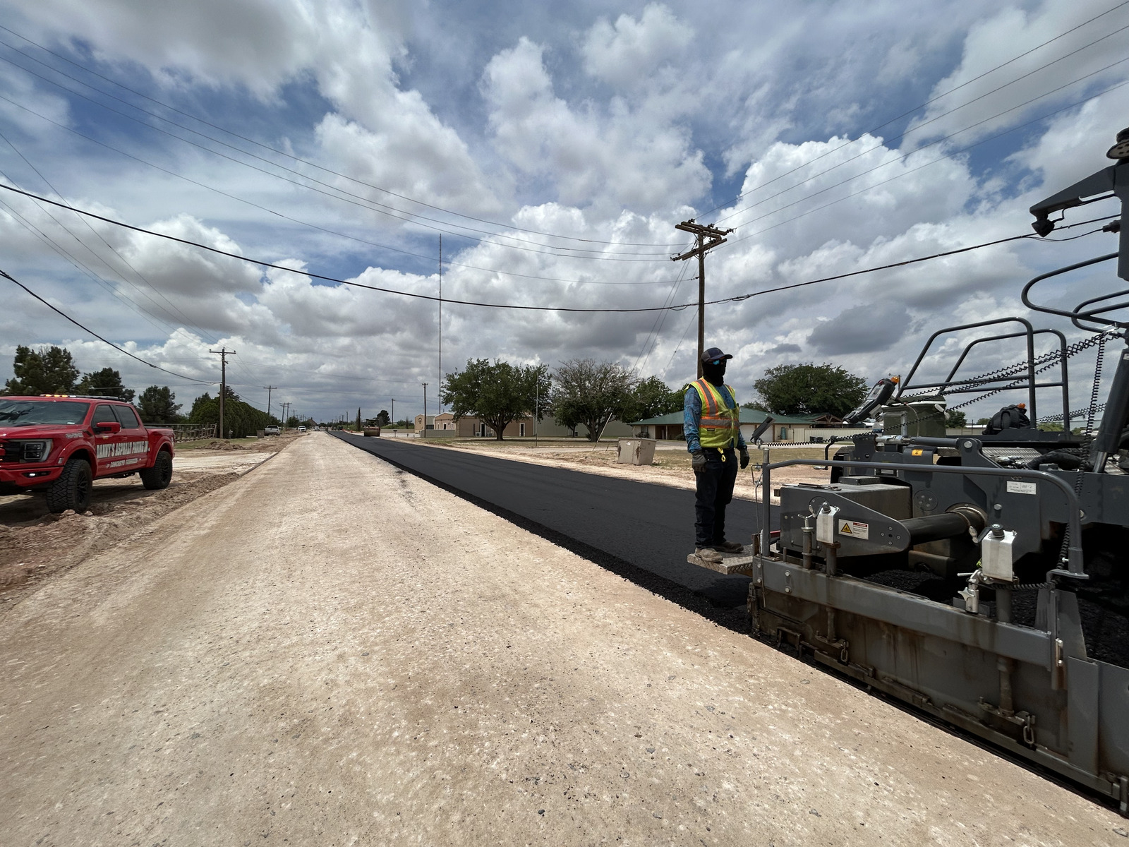 Aerial view of a freshly paved institutional asphalt parking lot with clearly marked white parking lines, directional arrows, and designated parking stalls adjacent to a commercial or educational building.