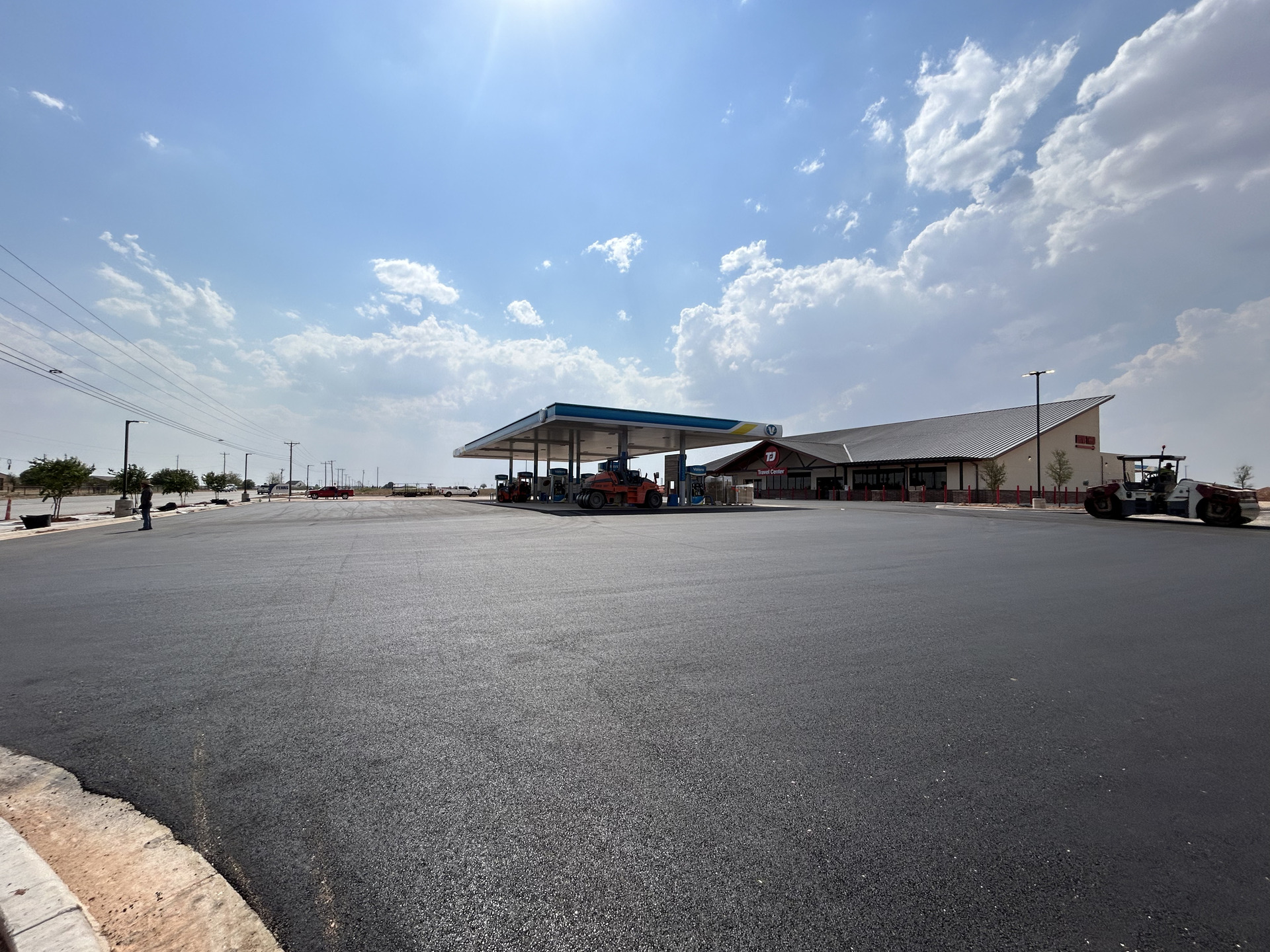 Aerial view of a freshly paved institutional asphalt parking lot with clearly marked white parking lines, directional arrows, and designated parking stalls adjacent to a commercial or educational building.
