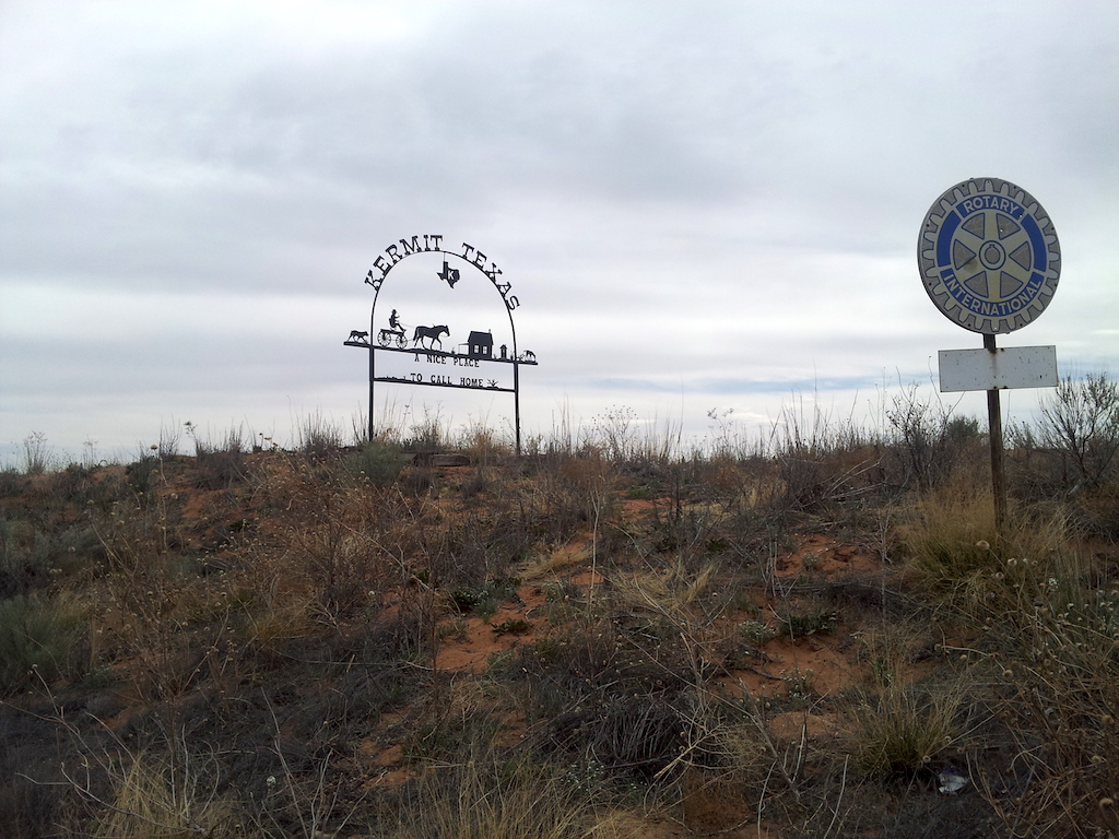 Aerial view of a freshly paved institutional asphalt parking lot with clearly marked white parking lines, directional arrows, and designated parking stalls adjacent to a commercial or educational building.