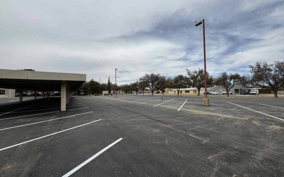 Large industrial parking lot with freshly paved asphalt, newly painted parking lines, and covered parking structure under an overcast sky.