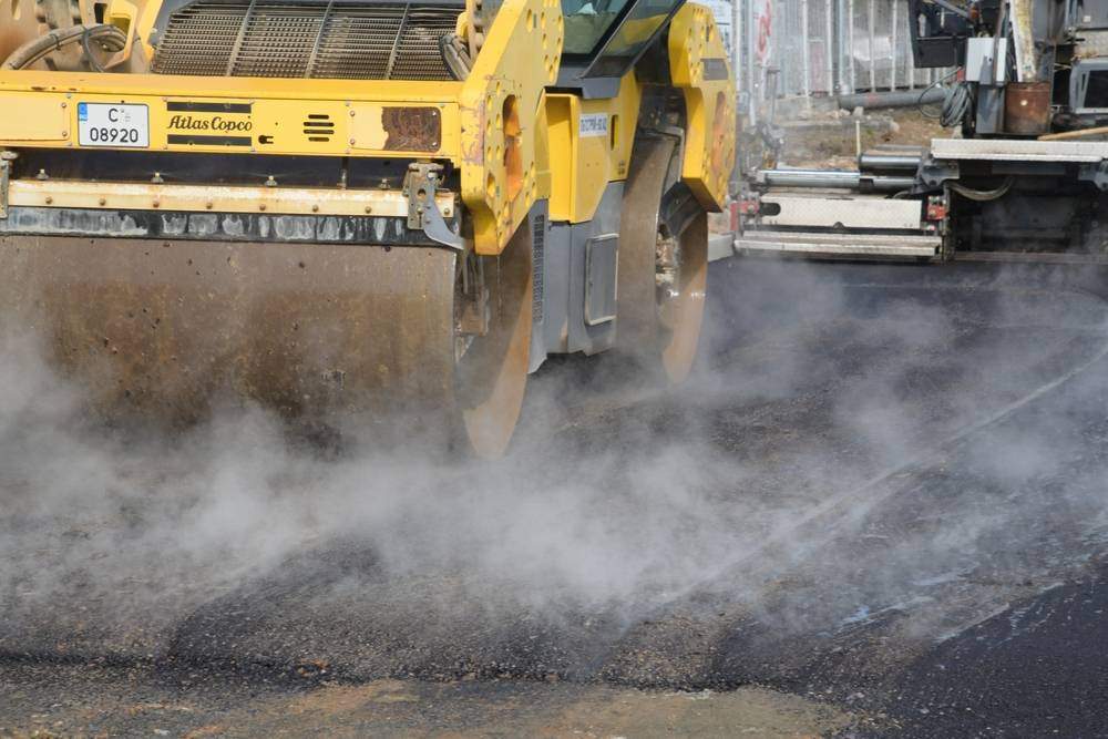 Close-up of an asphalt roller compacting a freshly installed asphalt overlay, with steam rising from the hot pavement during a commercial paving project to improve surface durability and extend pavement life.