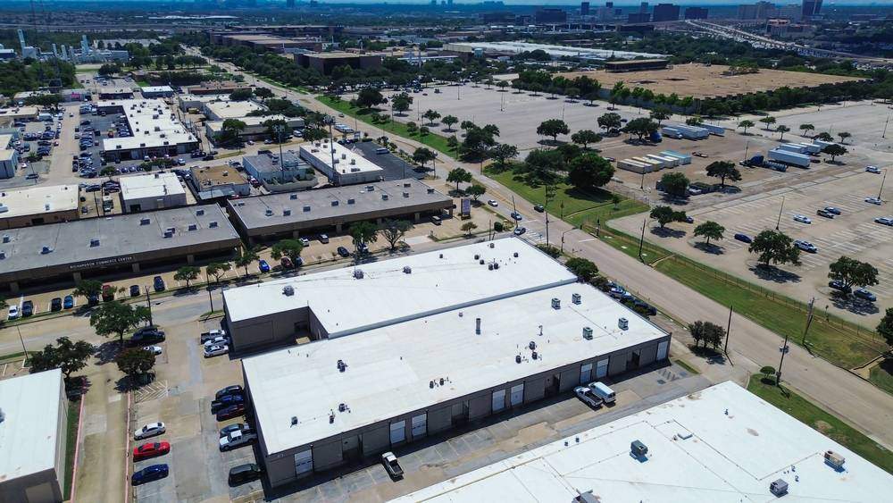 Aerial view of a freshly paved institutional asphalt parking lot with clearly marked white parking lines, directional arrows, and designated parking stalls adjacent to a commercial or educational building.